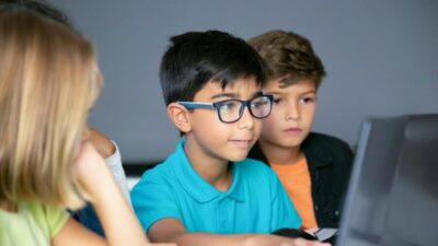 asian boy typing laptop keyboard classmates sitting table watching him doing task together e1745671955461